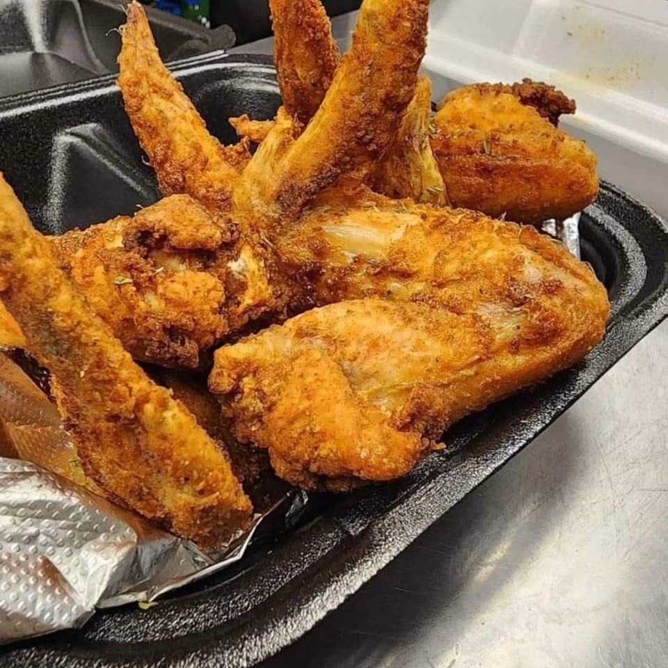 Crispy, golden-brown fried chicken wings and drumsticks in a black takeout container from Southern Soul Cafe.