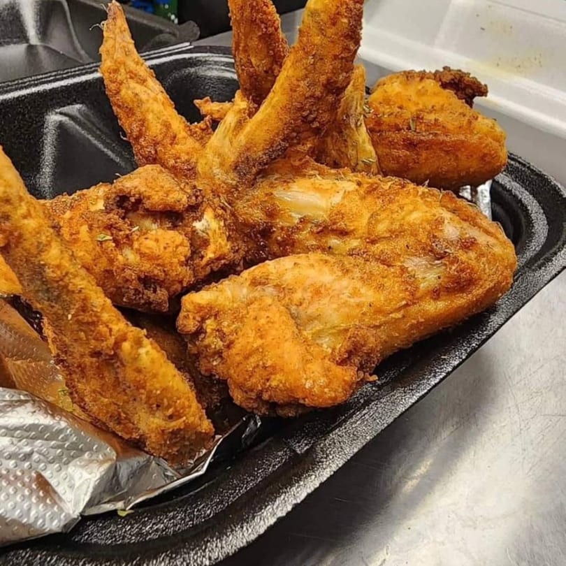 Crispy, golden-brown fried chicken wings and drumsticks in a black takeout container from Southern Soul Cafe.