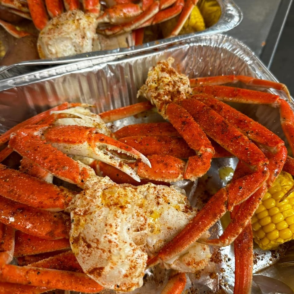 Two foil pans filled with seasoned crab legs, corn on the cob, and potatoes from Southern Soul Cafe.