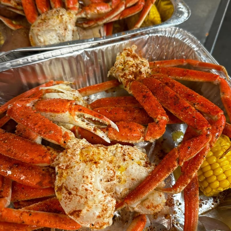 Two foil pans filled with seasoned crab legs, corn on the cob, and potatoes from Southern Soul Cafe.