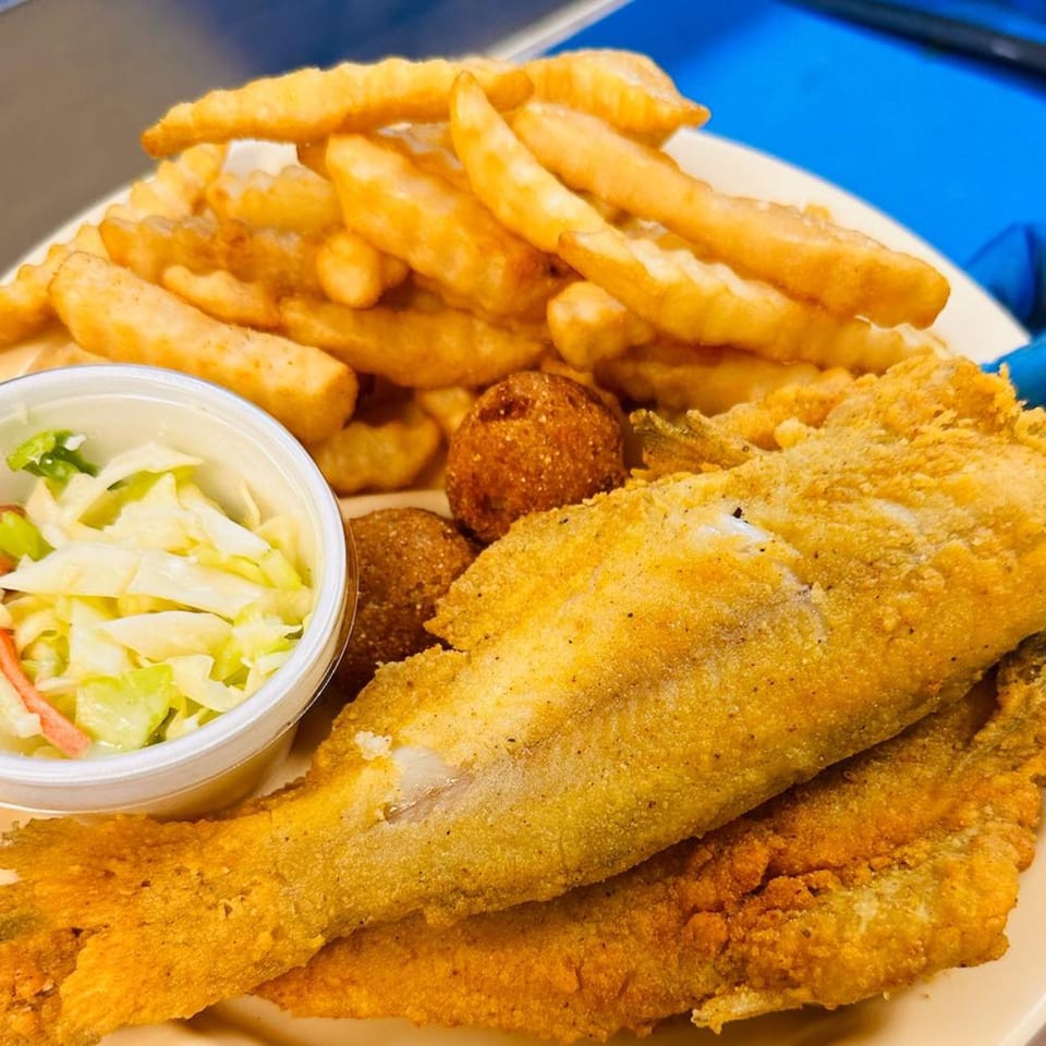 Crispy fried fish, crinkle-cut fries, hush puppies, and coleslaw on a plate at Southern Soul Cafe.