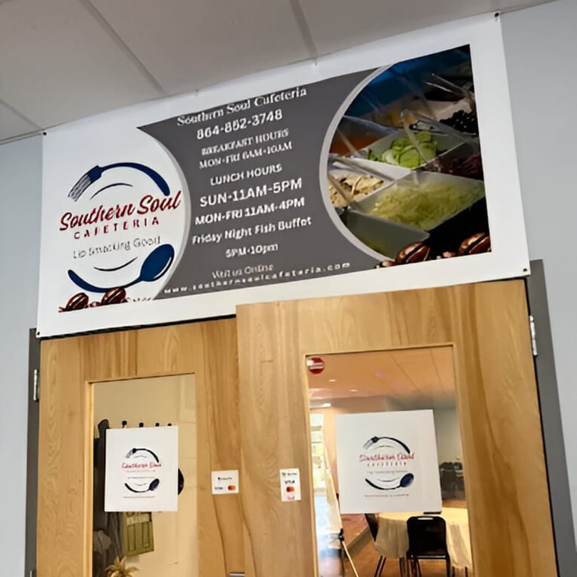A large banner for Southern Soul Cafeteria with hours and a salad bar image, above wooden doors.