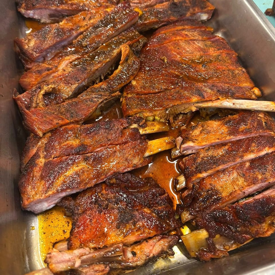Close-up of glistening, saucy, sliced BBQ ribs in a metal pan, ready to be served.